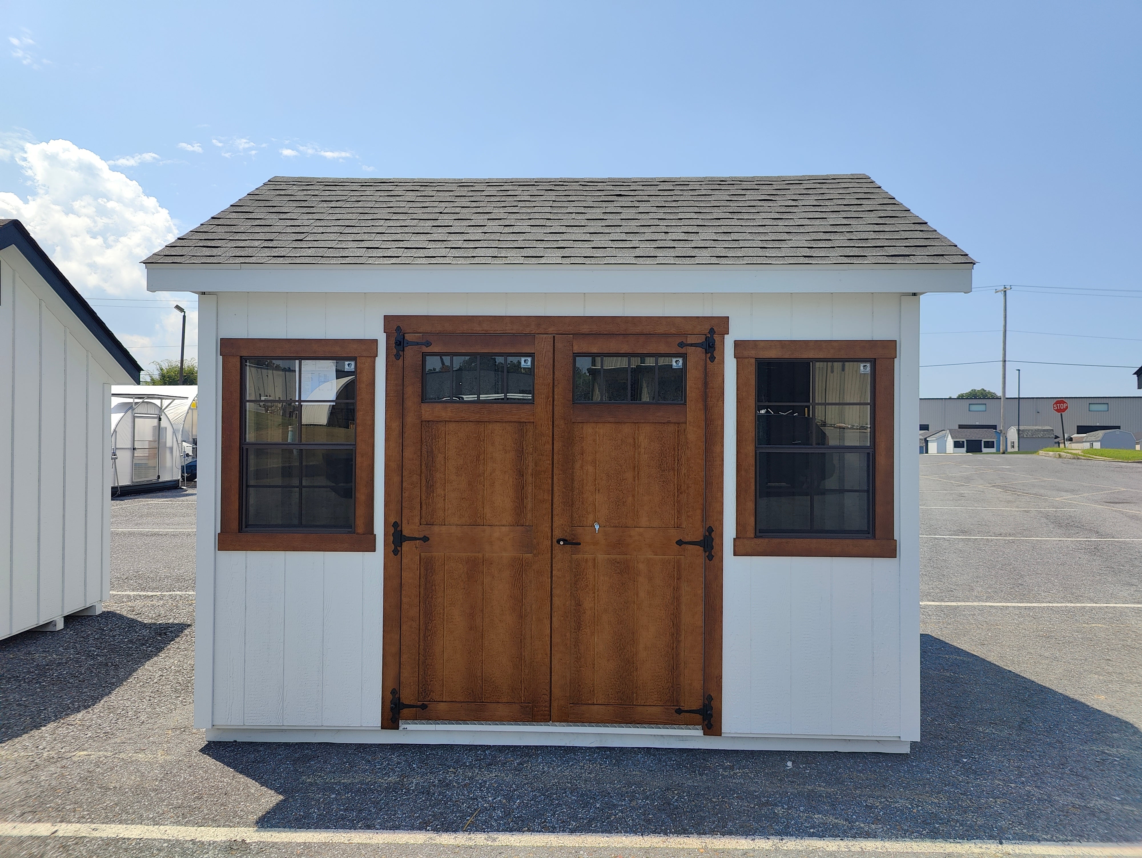 Small wooden shed with white walls, brown doors, and windows on a clear day.